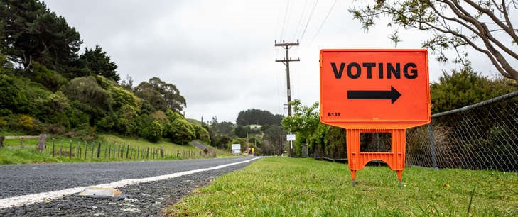 An orange sign that says 'voting' with an arrow in a rural road setting